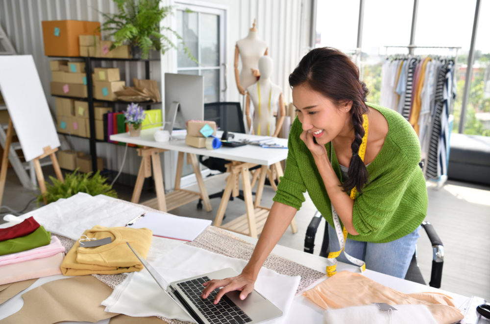 A women looking at her laptop while talking on the phone.